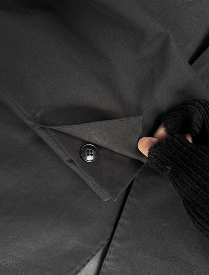 Close-up of a black coat with a button being adjusted by a hand wearing a textured glove.