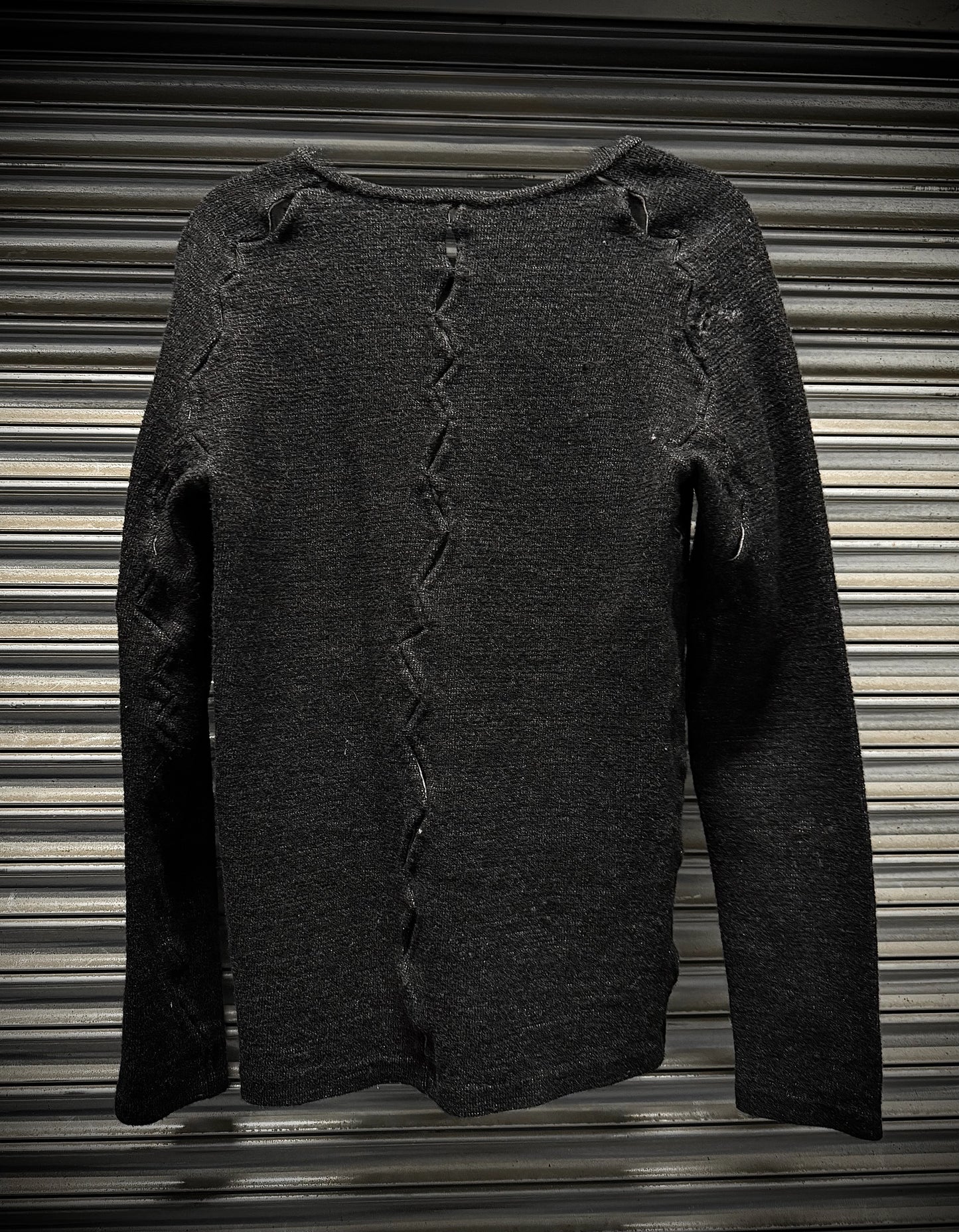 Dark gray sweater with distressed details on a corrugated metal background