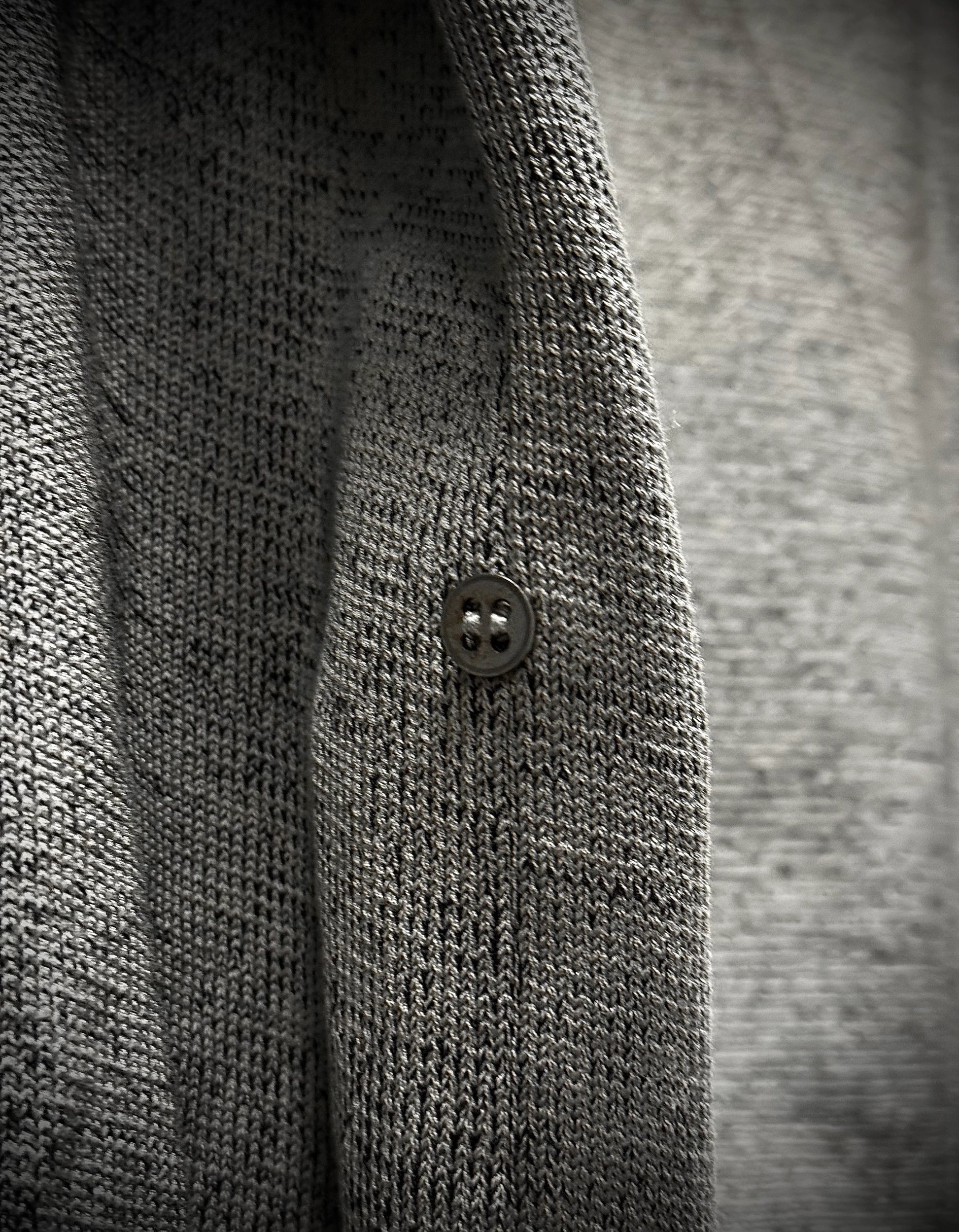 Close-up of a textured gray sweater with a button on a blurred background