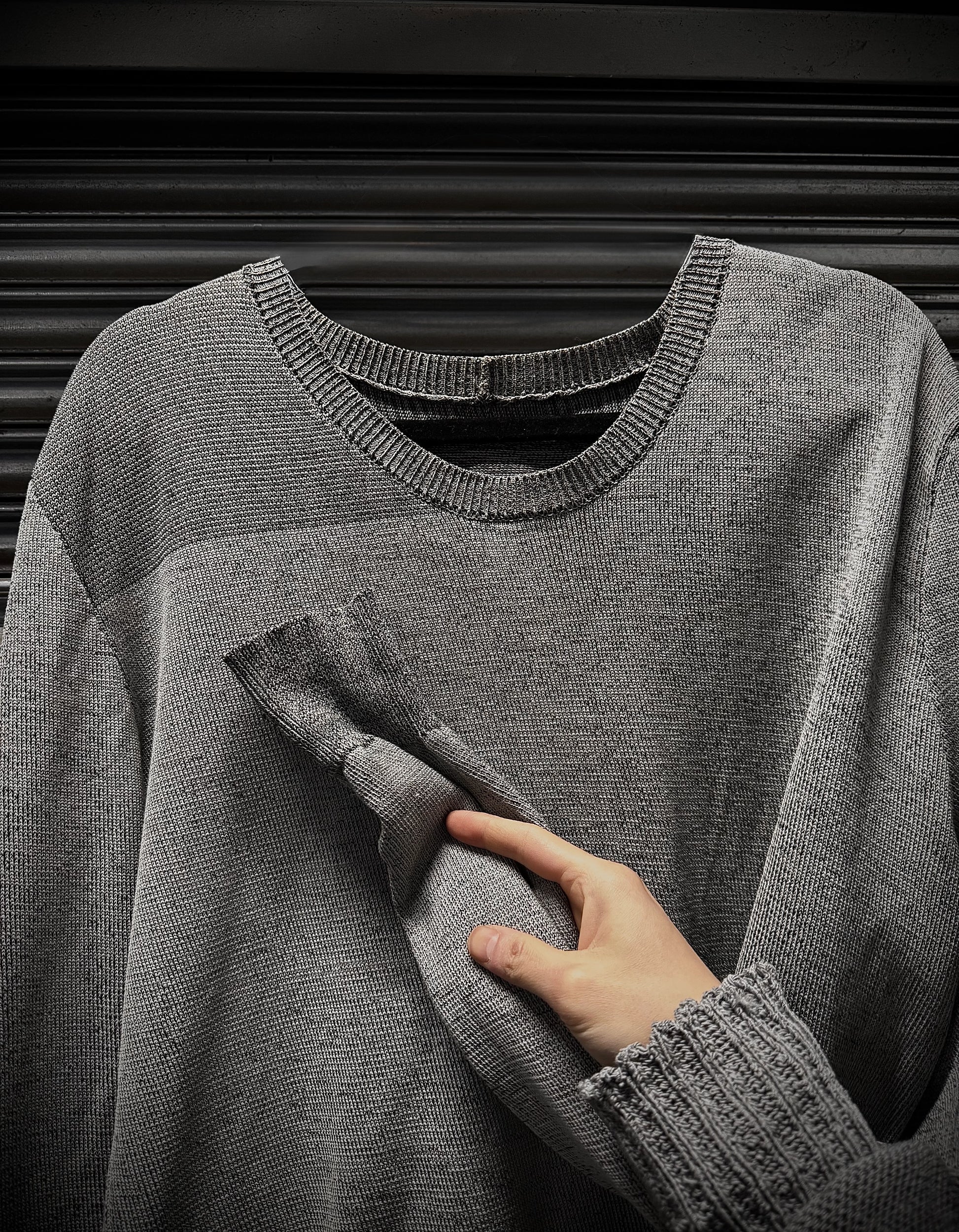 Gray sweater with a hand touching the fabric against a dark background