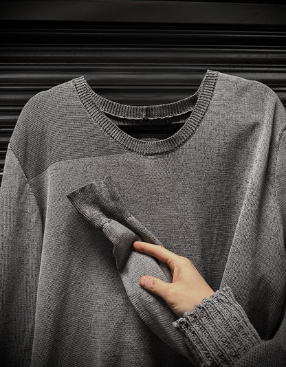 Gray sweater with a hand touching the fabric against a dark background