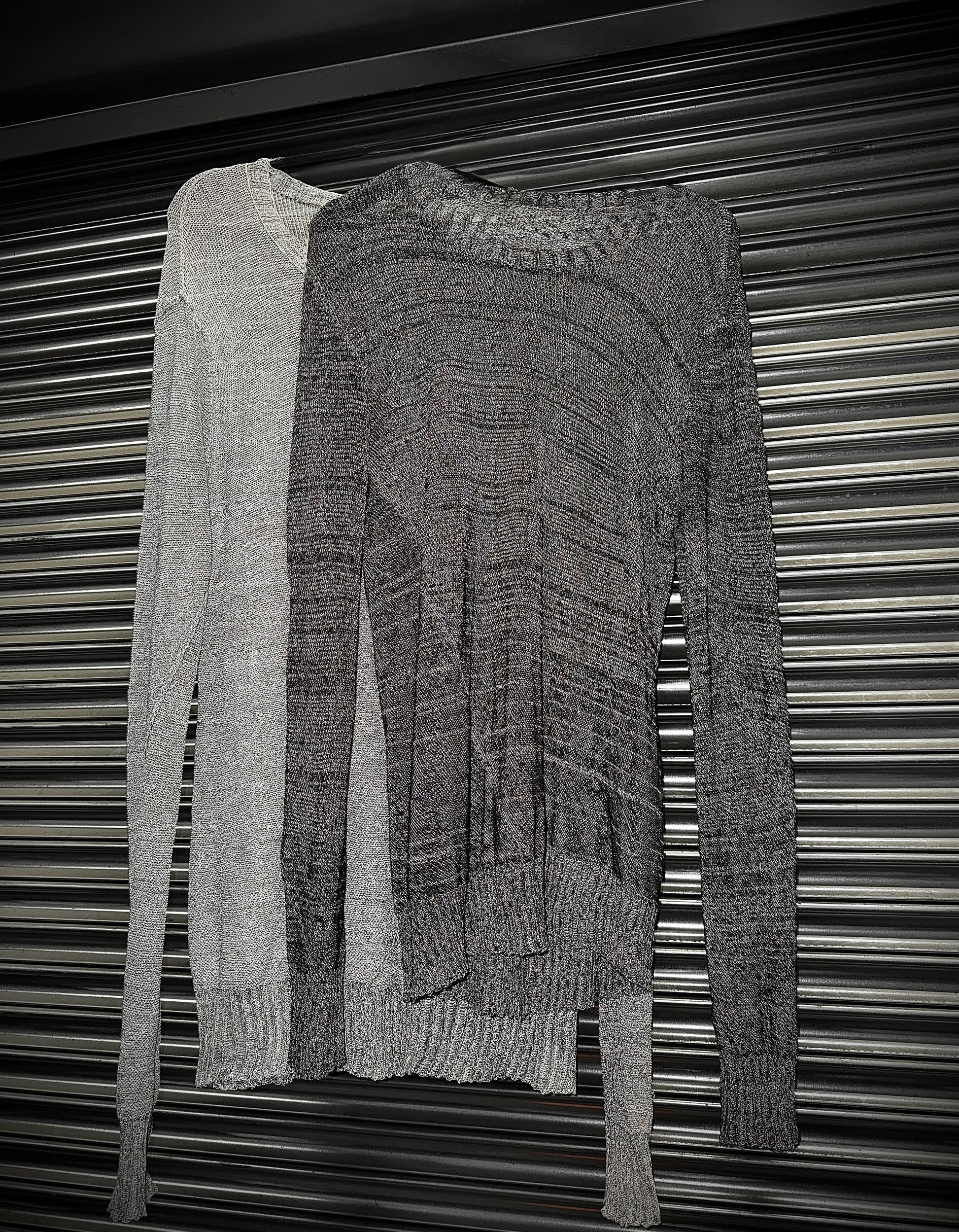 Two knitted sweaters, one gray and one black, draped over a metallic surface.