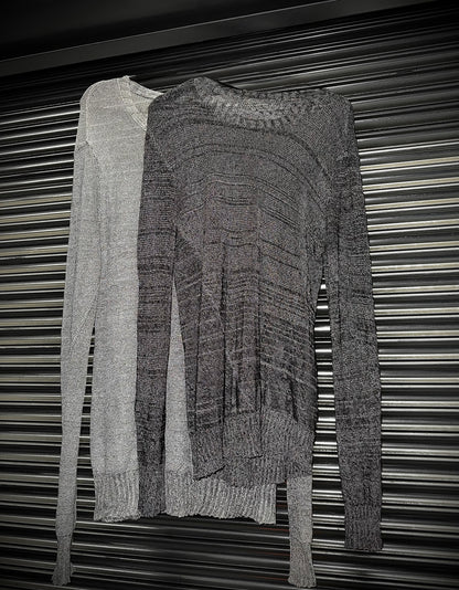Two knitted sweaters, one gray and one black, draped over a metallic surface.