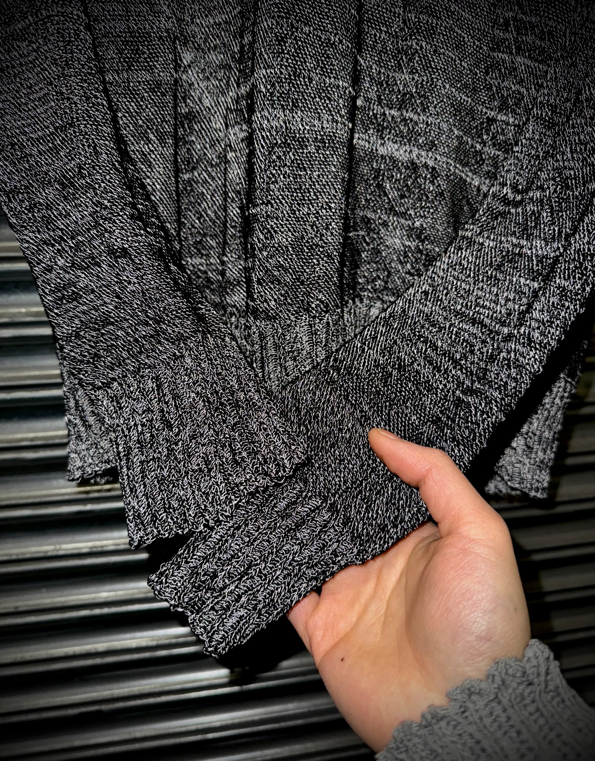 Hand holding a folded gray sweater against a metallic background