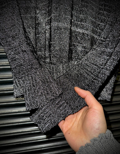Hand holding a folded gray sweater against a metallic background