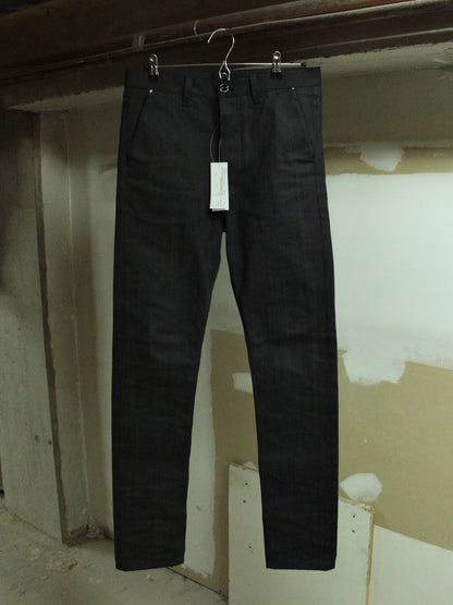 Black pants hanging on a hook against a plain wall.