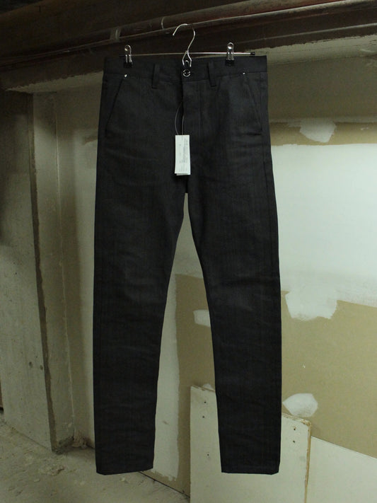 Black pants hanging on a hook against a plain wall.