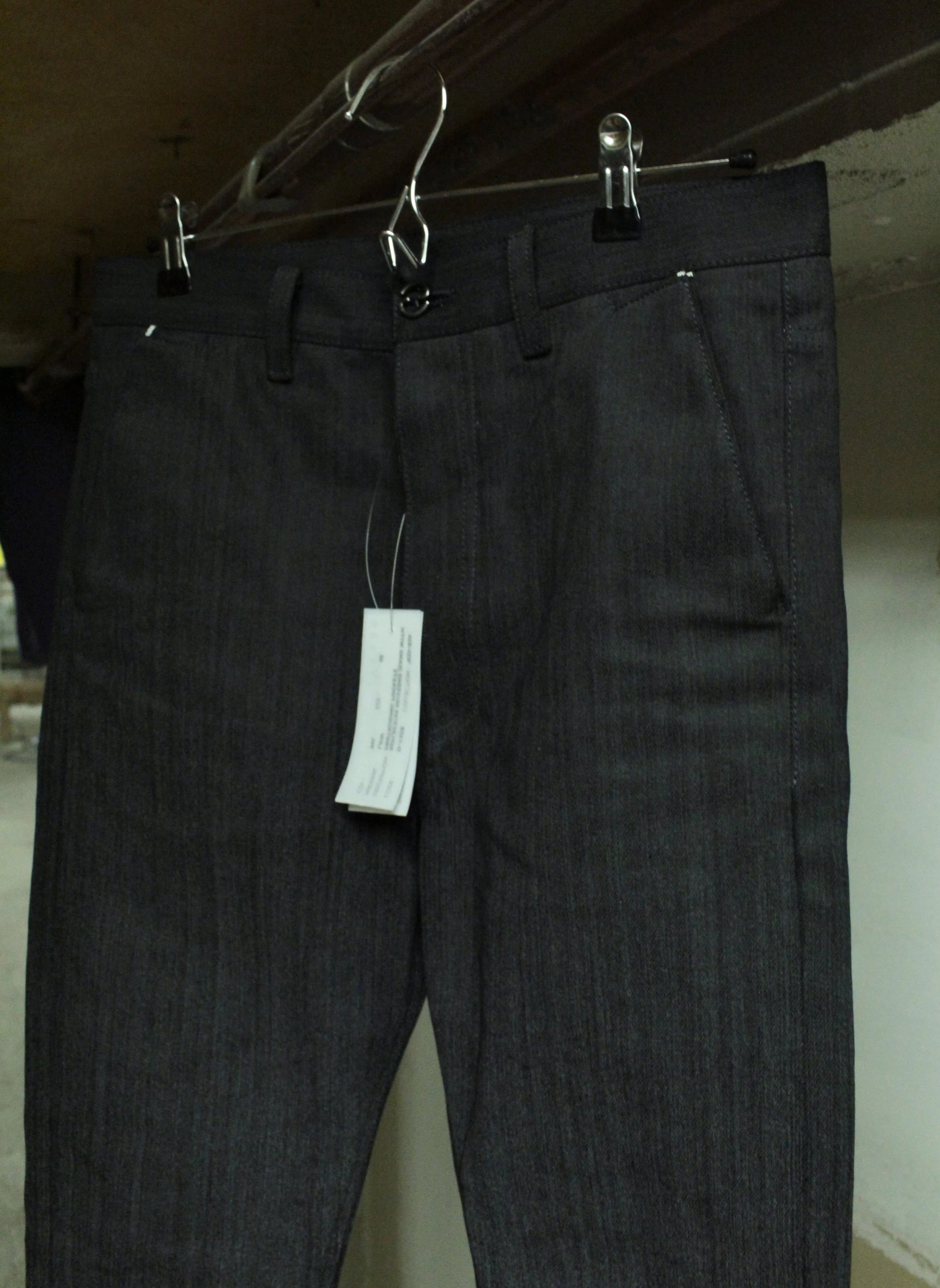 Dark gray pants with a tag hanging on a hook against a plain background