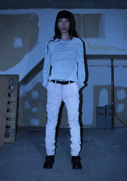 Person wearing a light gray sweater and pants in a dark room with minimal background