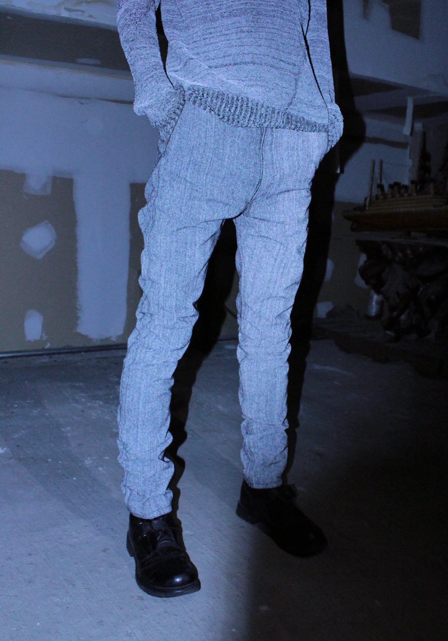Person wearing a reflective knit sweater and pants in a dimly lit room.