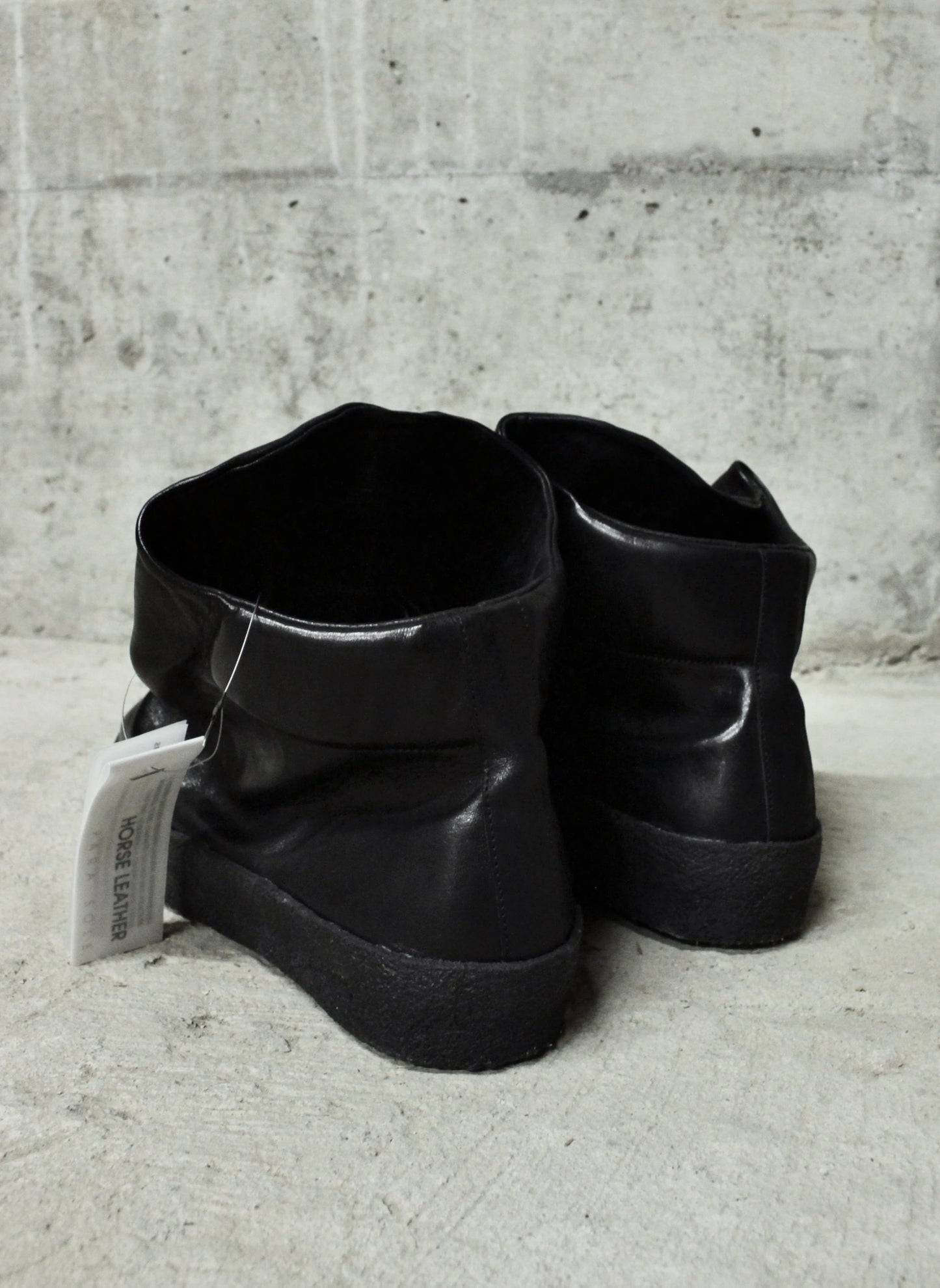 Pair of black leather boots on a concrete floor with a gray wall background