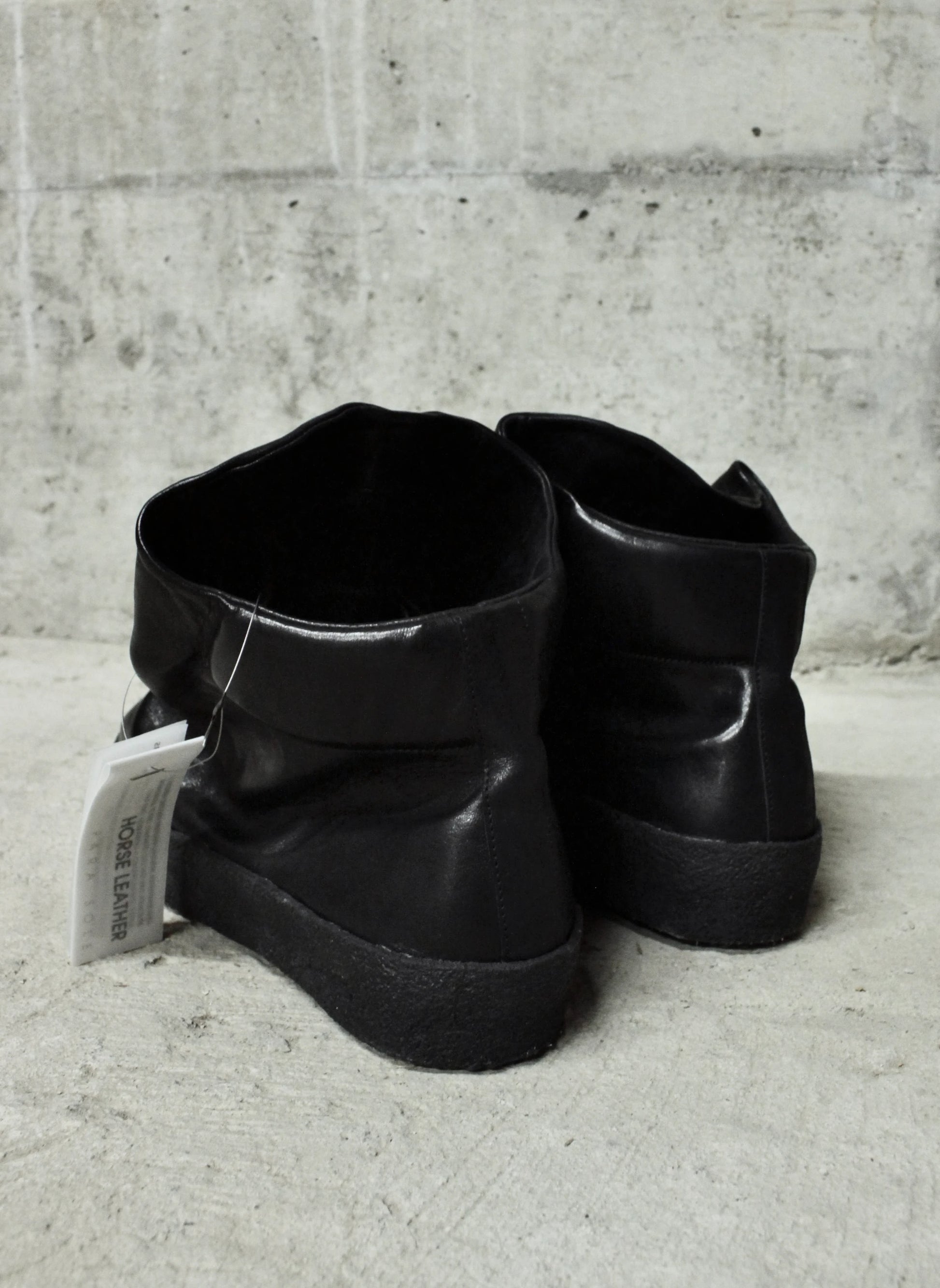 Pair of black leather boots on a concrete floor with a gray wall background