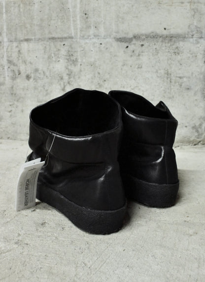 Pair of black leather boots on a concrete floor with a gray wall background