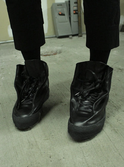 Black high-top sneakers on a concrete floor with a blurred background