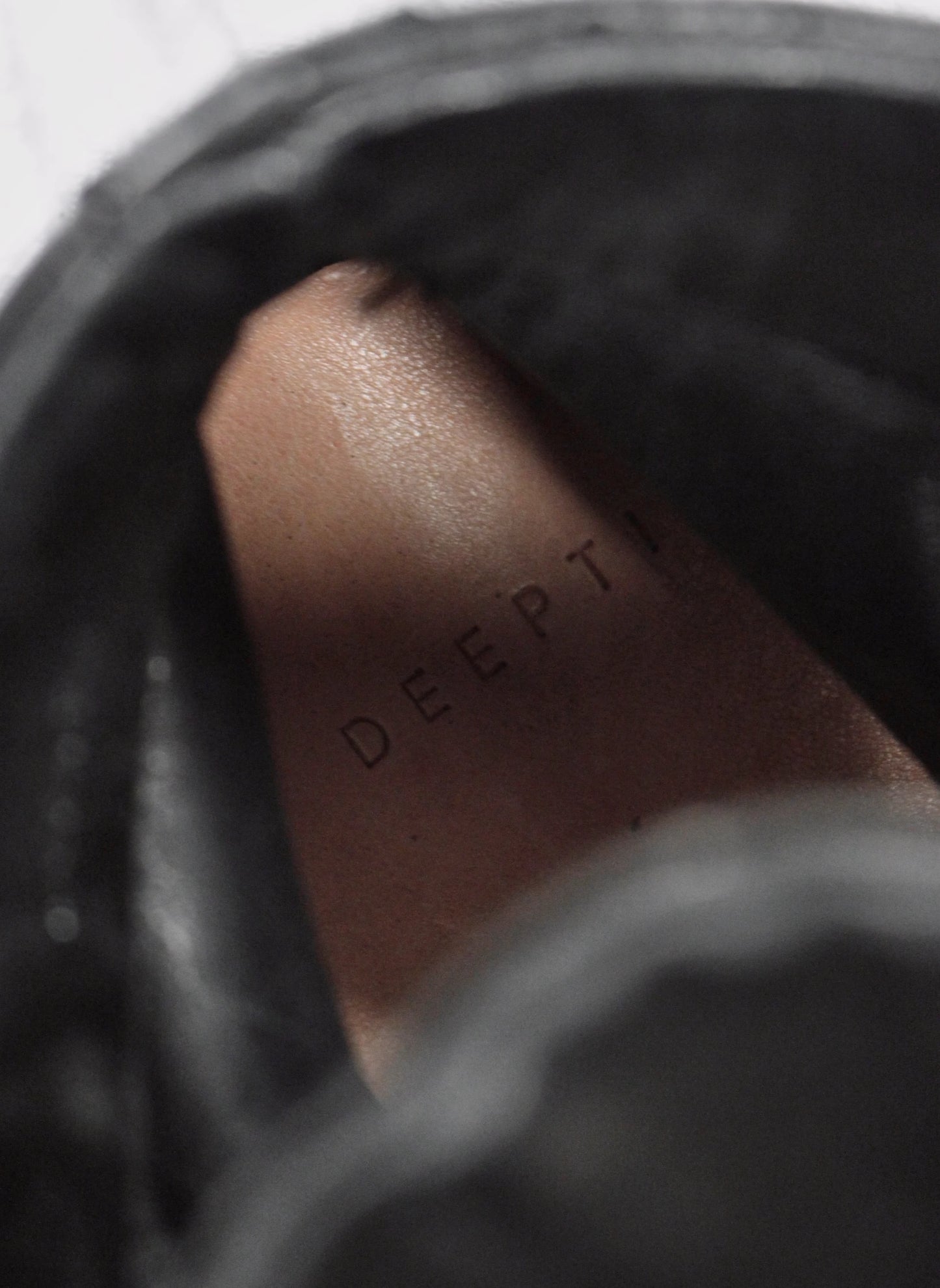 Close-up of a brown leather patch with 'DEEPTI' embossed on it, inside a black bag.