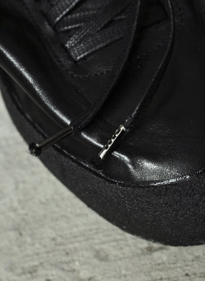Close-up of a black leather shoe with a lace on a concrete surface