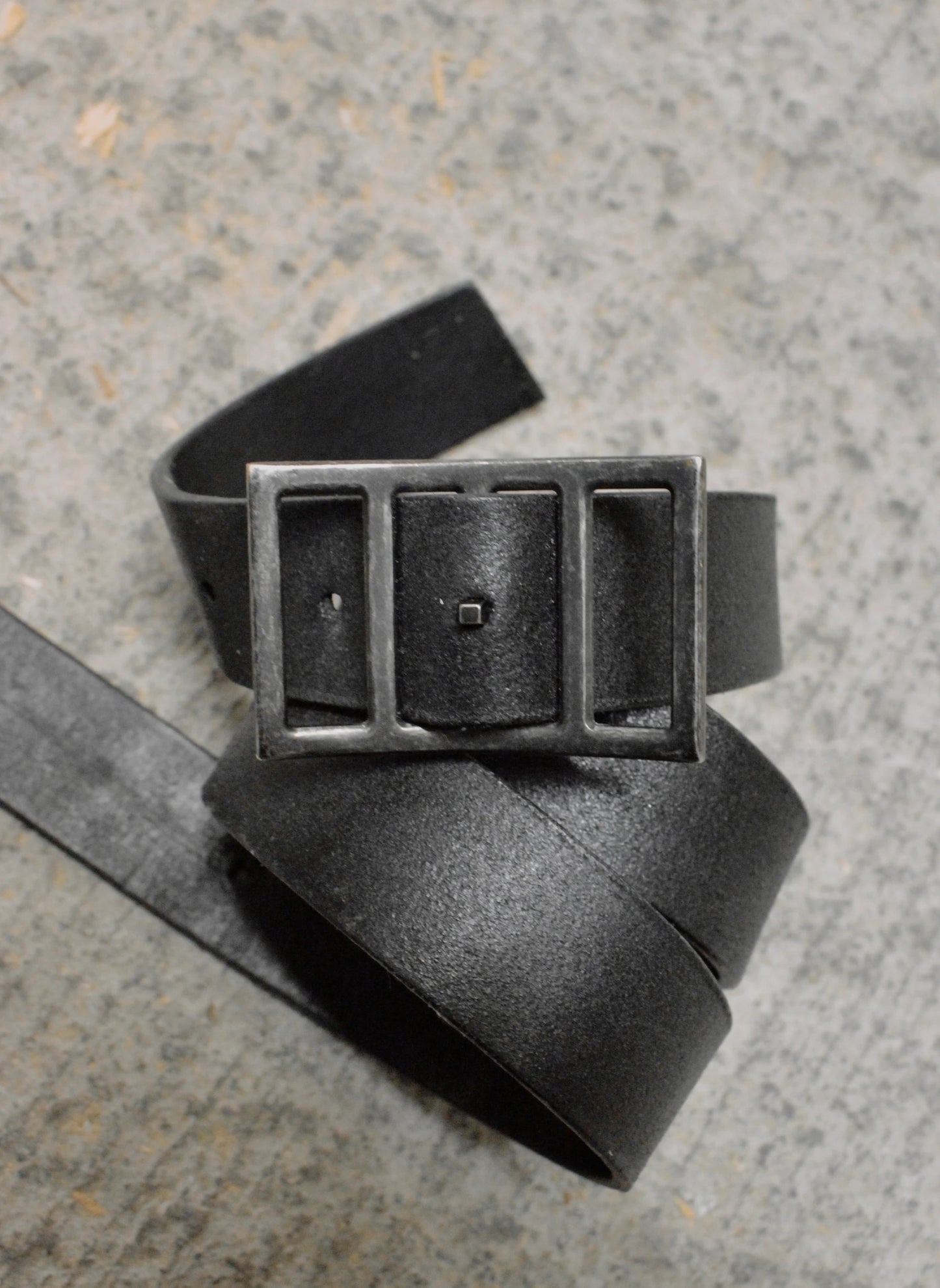 Black leather belt with a rectangular buckle on a textured surface