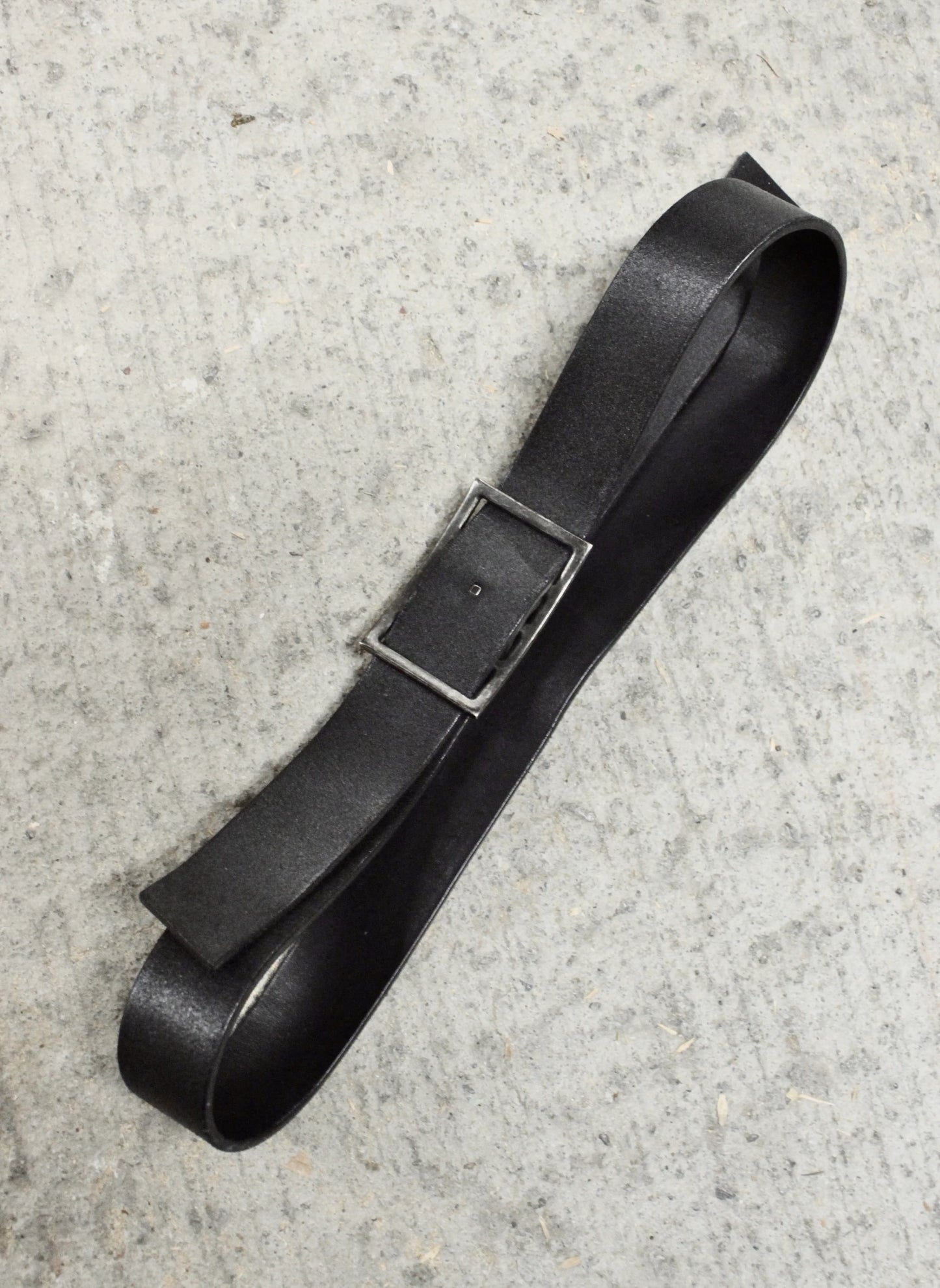 Black leather belt with a silver buckle on a gray concrete surface