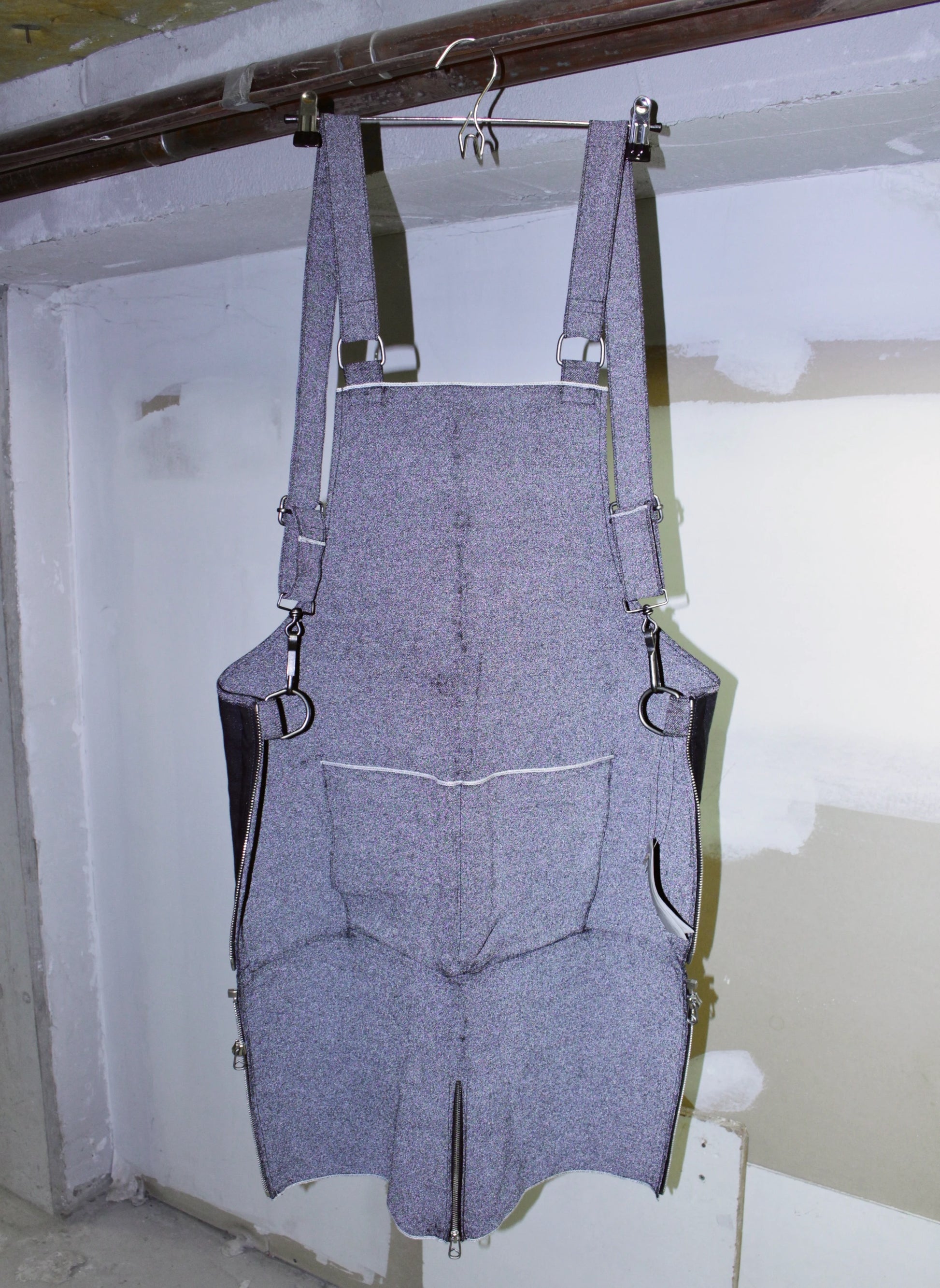 reflective denim overalls hanging on a hook against a white wall.
