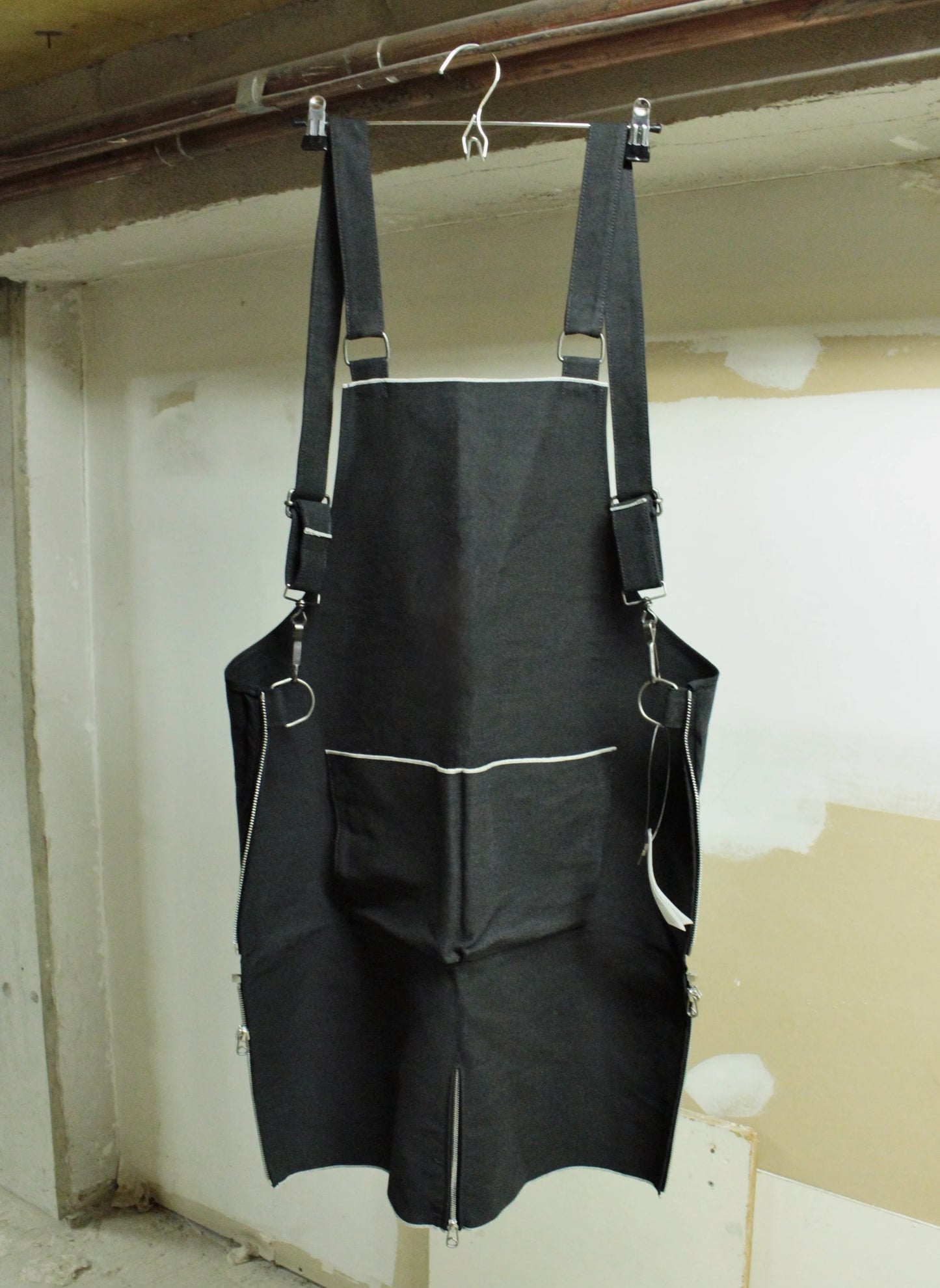 Black apron hanging on a hook against a plain wall.