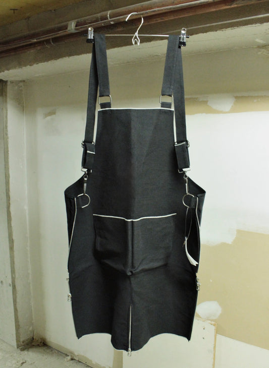 Black apron hanging on a hook against a plain wall.