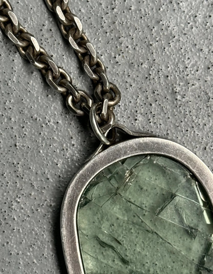 Necklace with a green stone pendant on a gray textured background