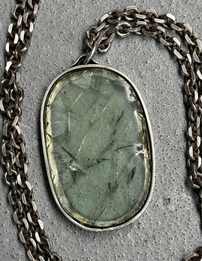 Necklace with a green stone pendant on a concrete surface