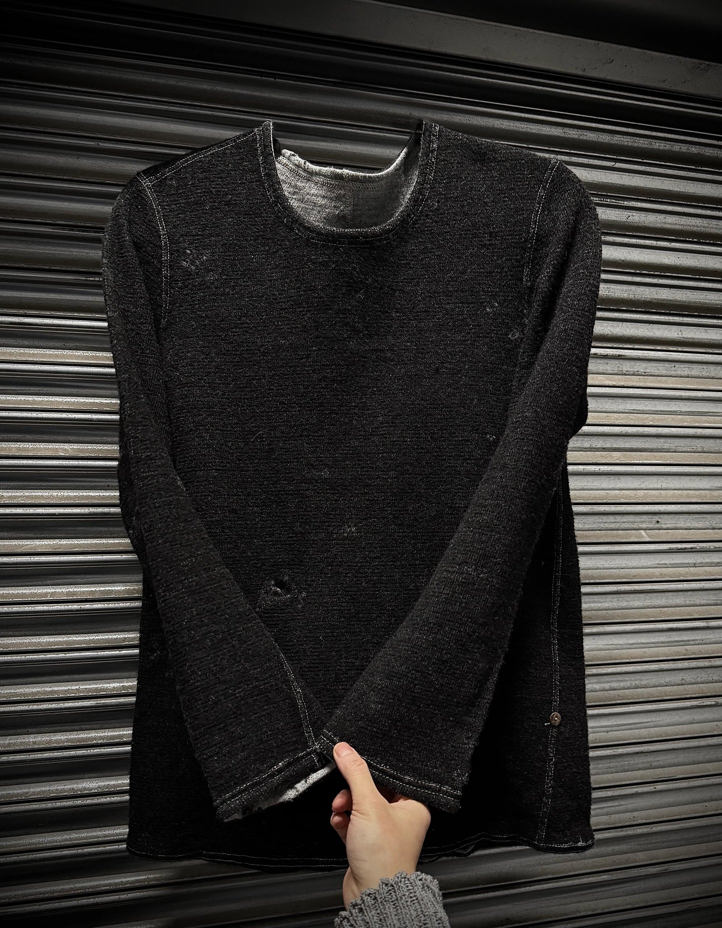 Dark gray long-sleeve shirt held by a hand against a metallic background