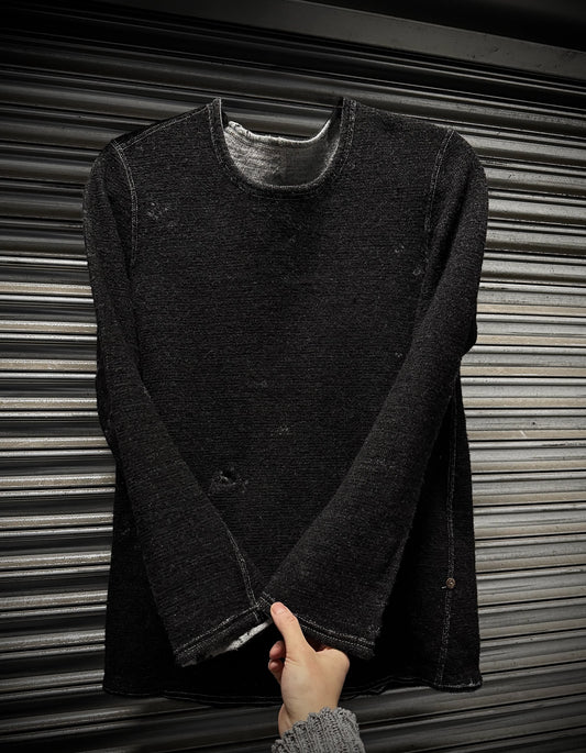 Dark gray long-sleeve shirt held by a hand against a metallic background