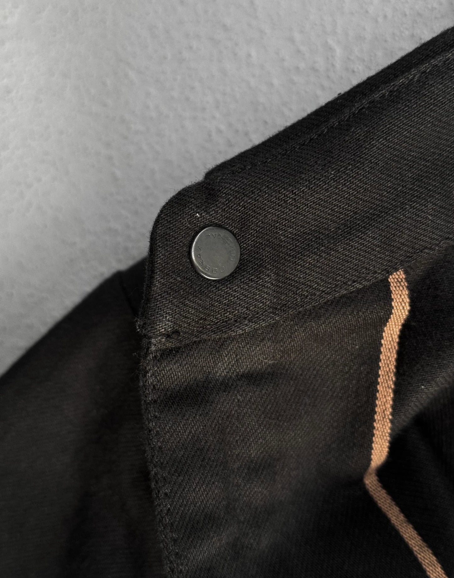 Close-up of a black jacket with a button and brown trim on a gray background