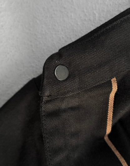 Close-up of a black jacket with a button and brown trim on a gray background