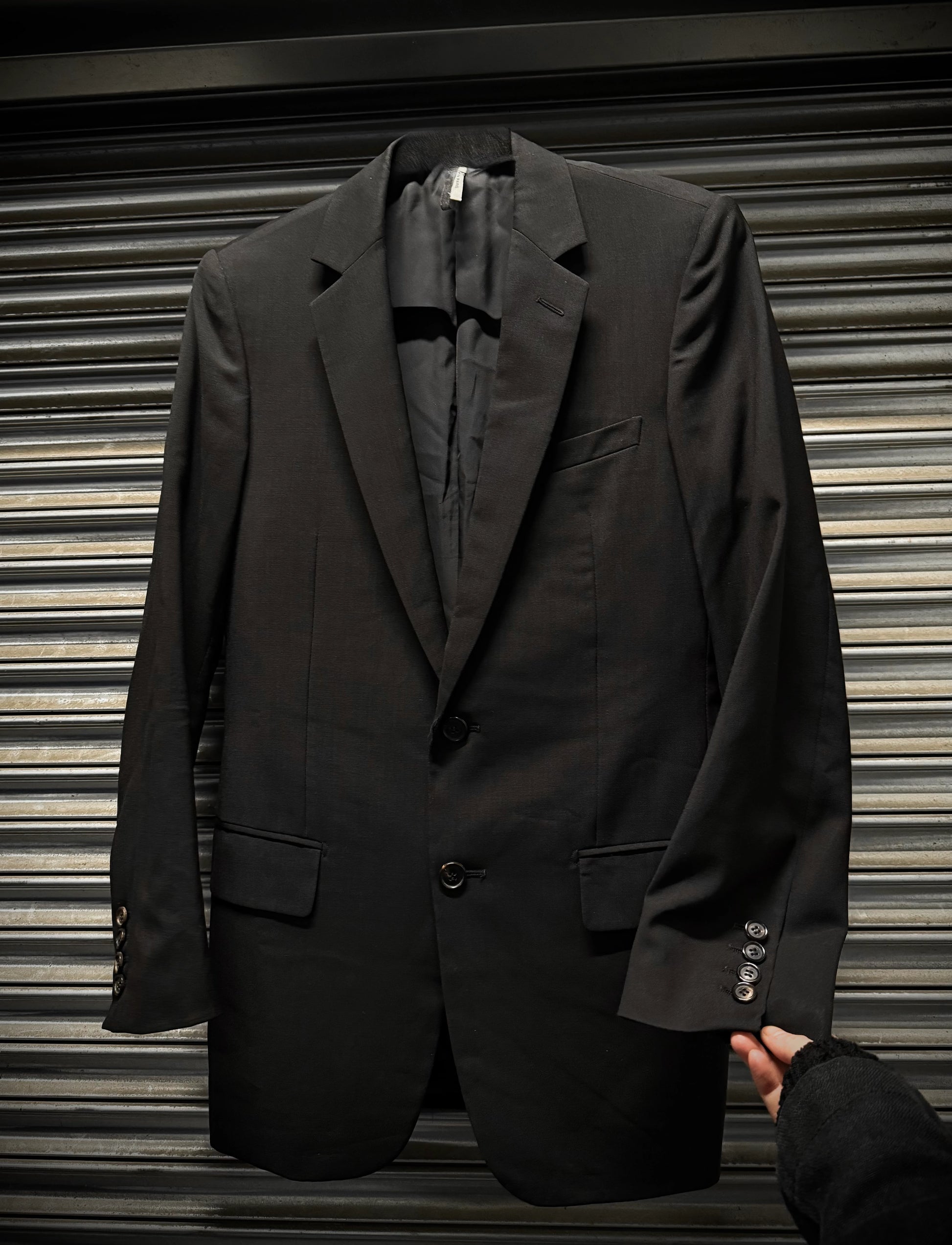 Black suit jacket held by a hand against a metallic shutter background