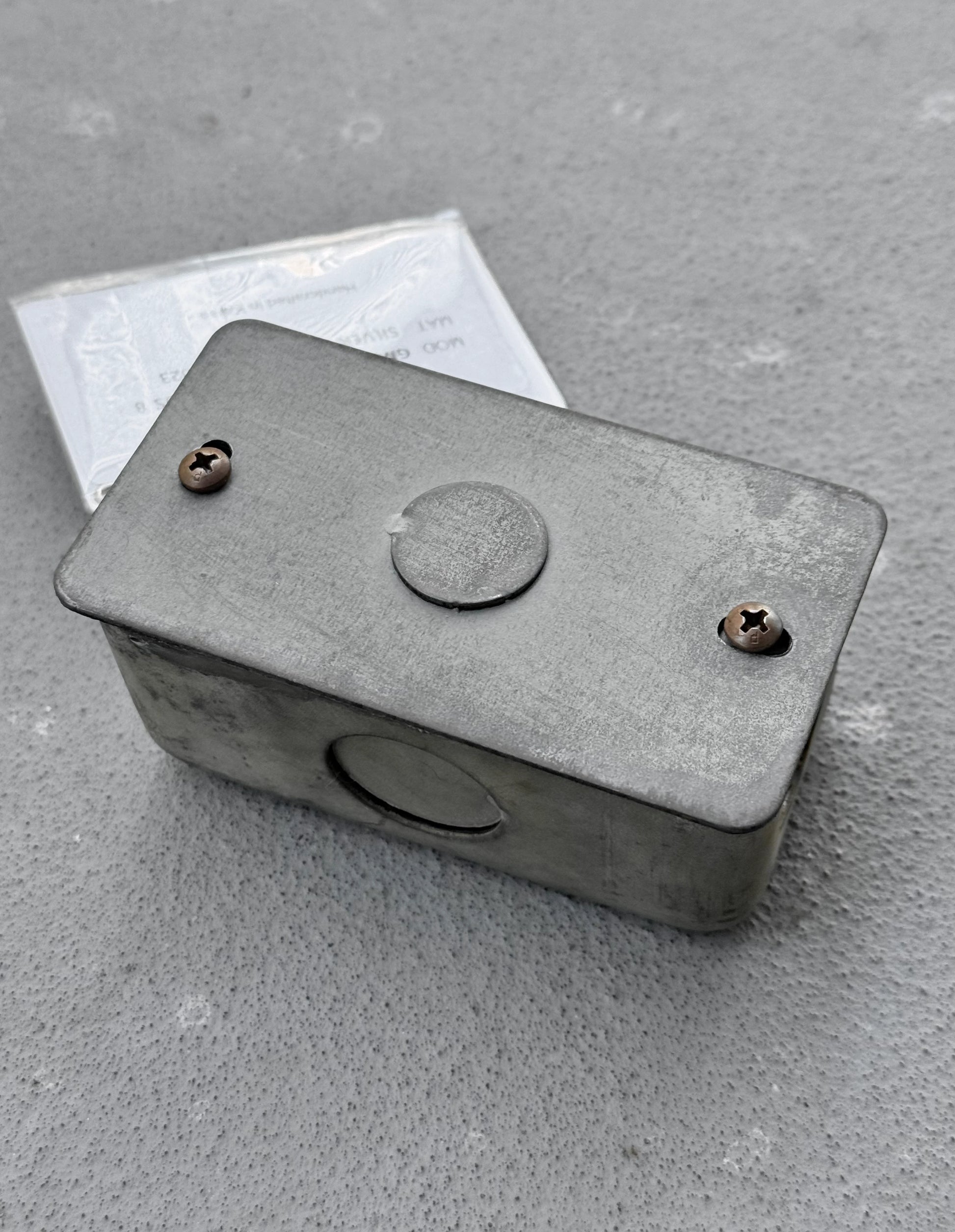 Metal box with screws on a gray concrete surface