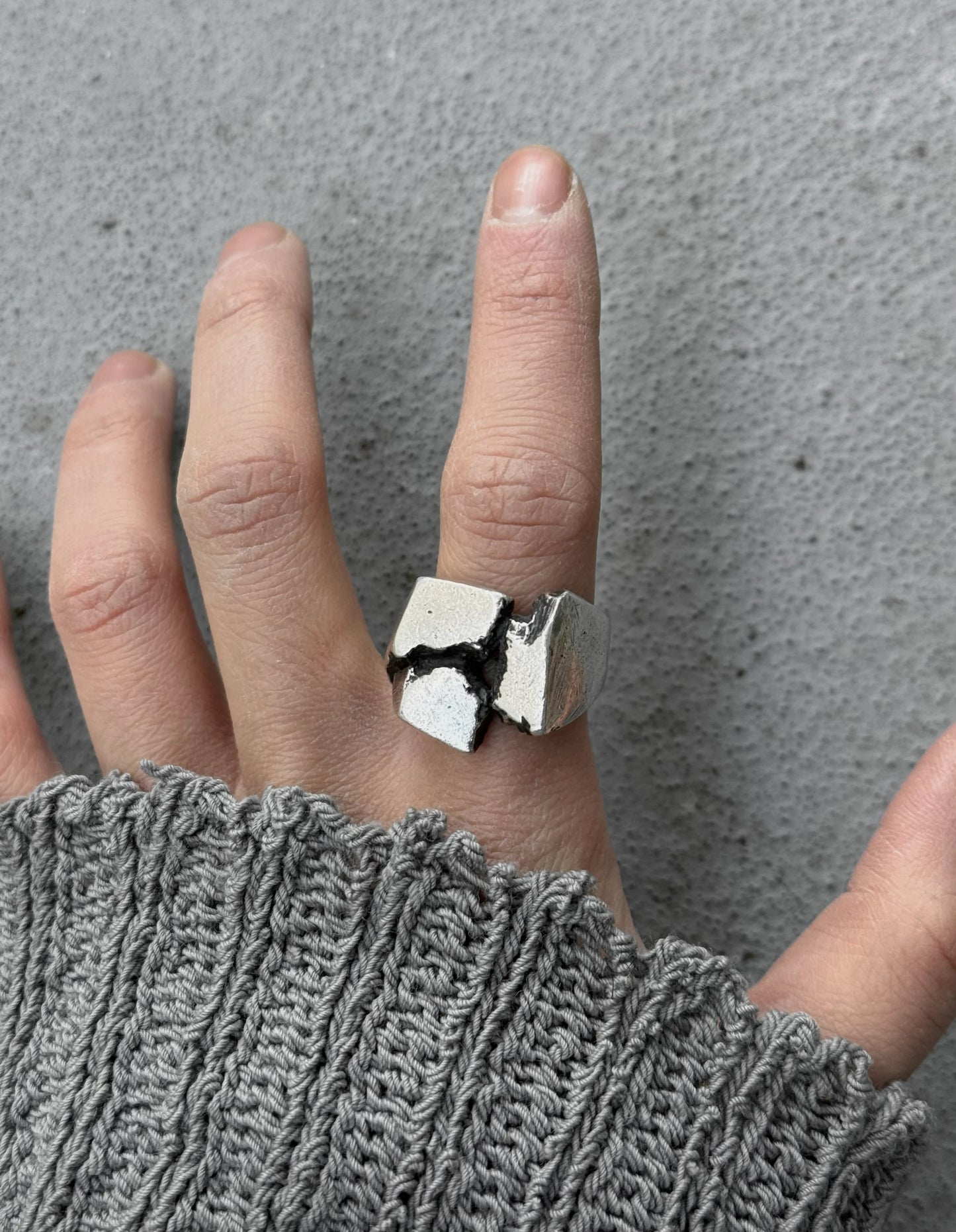 Hand wearing a silver ring with a unique design on a gray background