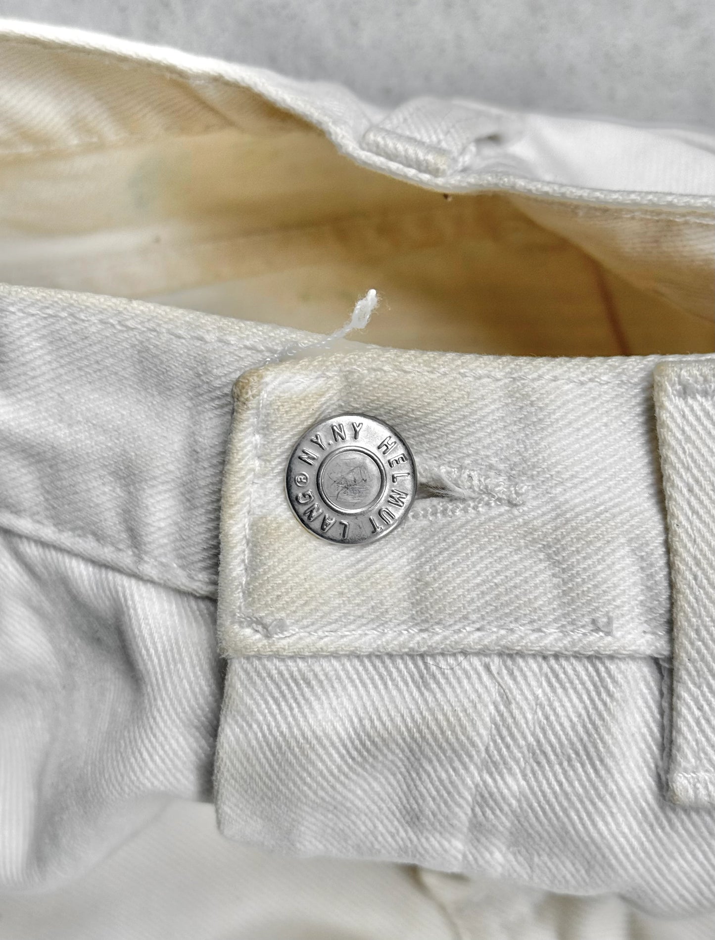 Close-up of a button on light-colored denim fabric with 'Helmut Lang' branding.