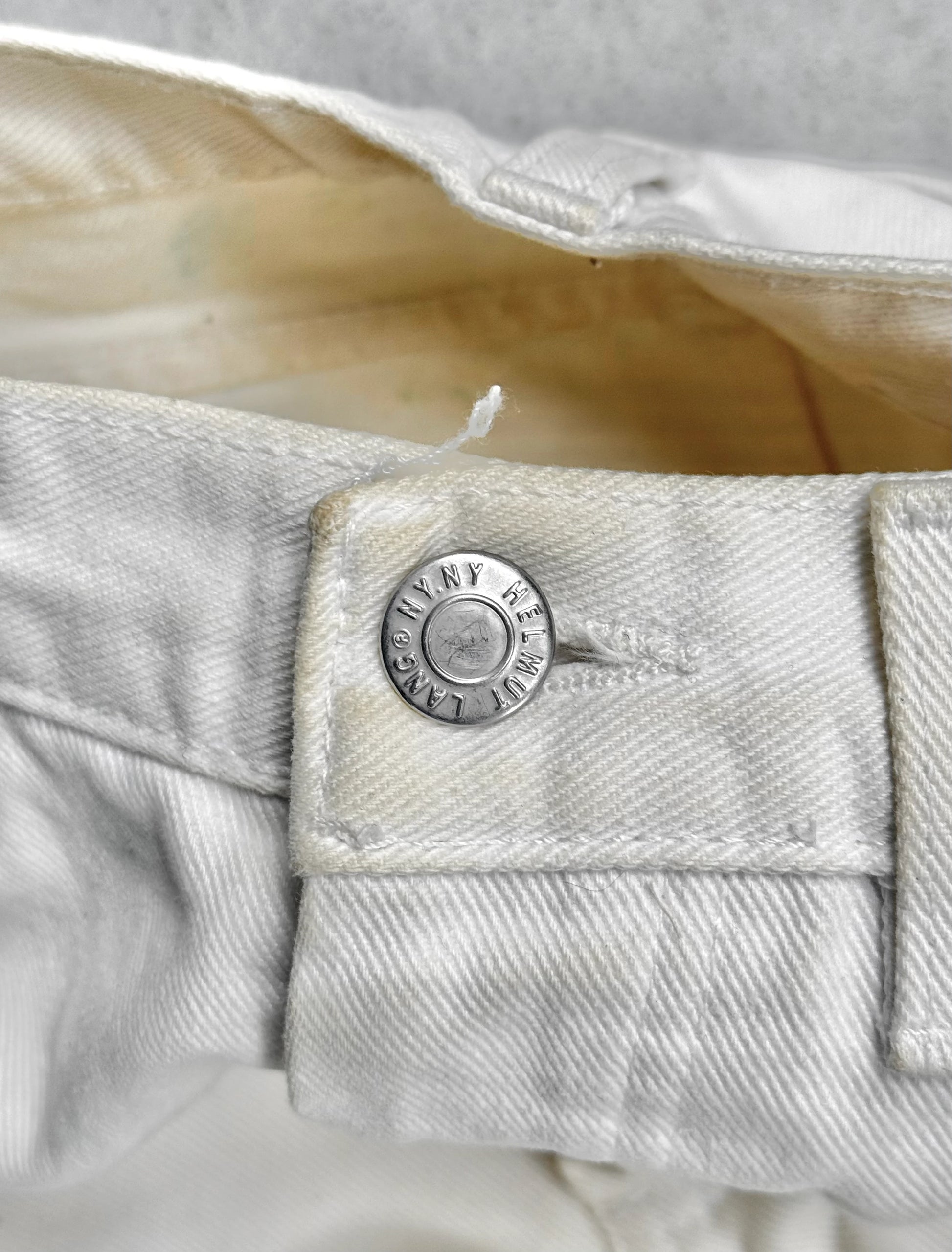 Close-up of a button on light-colored denim fabric with 'Helmut Lang' branding.