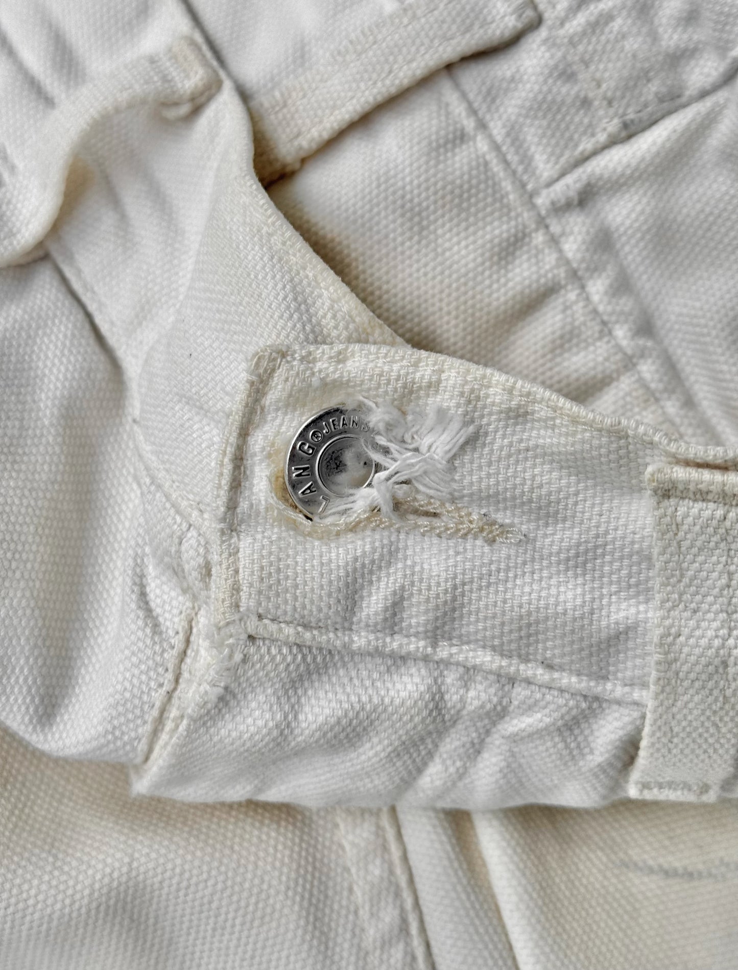 Close-up of a white denim jacket with a button and stitching detail.