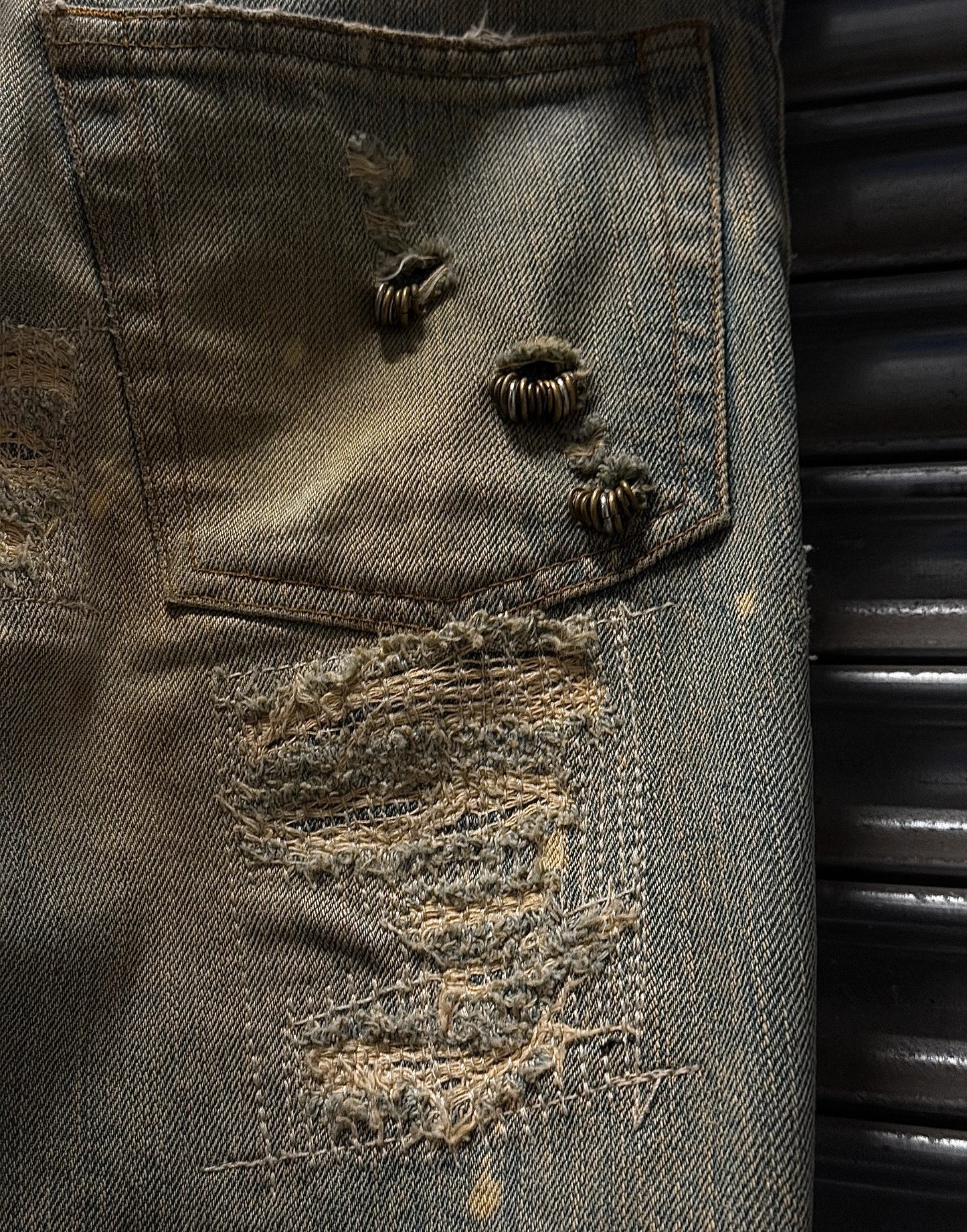 Close-up of a distressed denim pocket with buttons and lace trim.