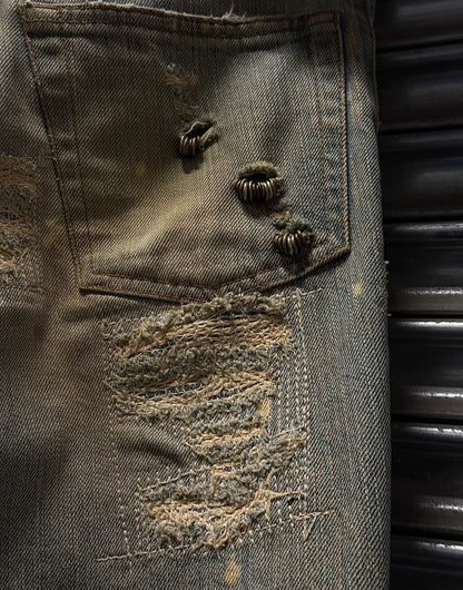 Close-up of a distressed denim pocket with buttons and lace trim.