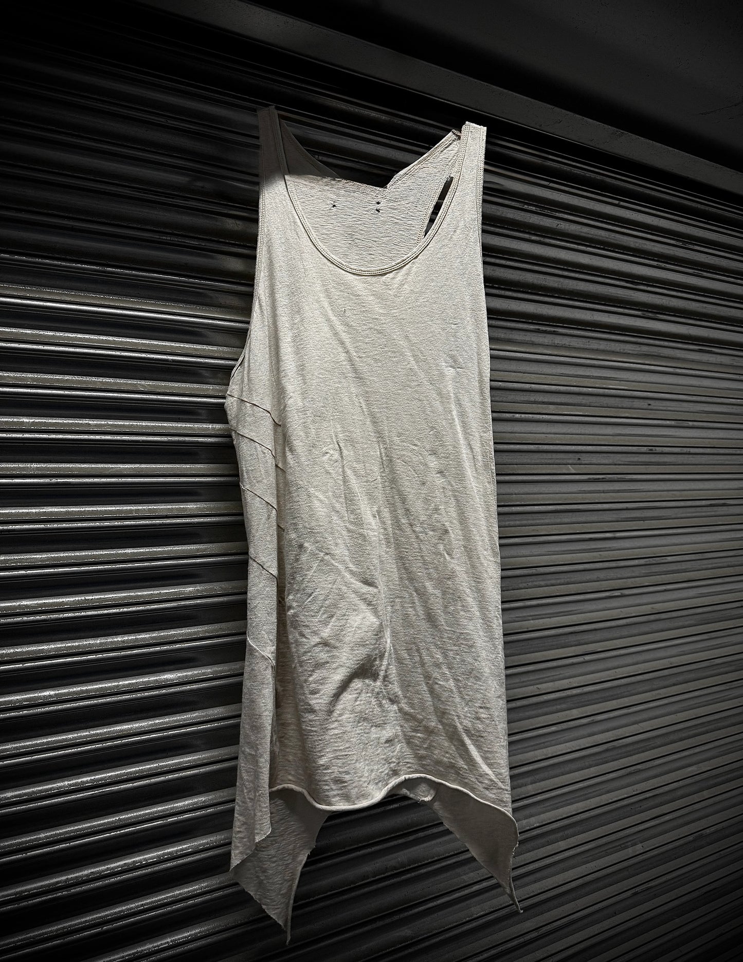 Light gray tank top hanging against a dark, textured wall.