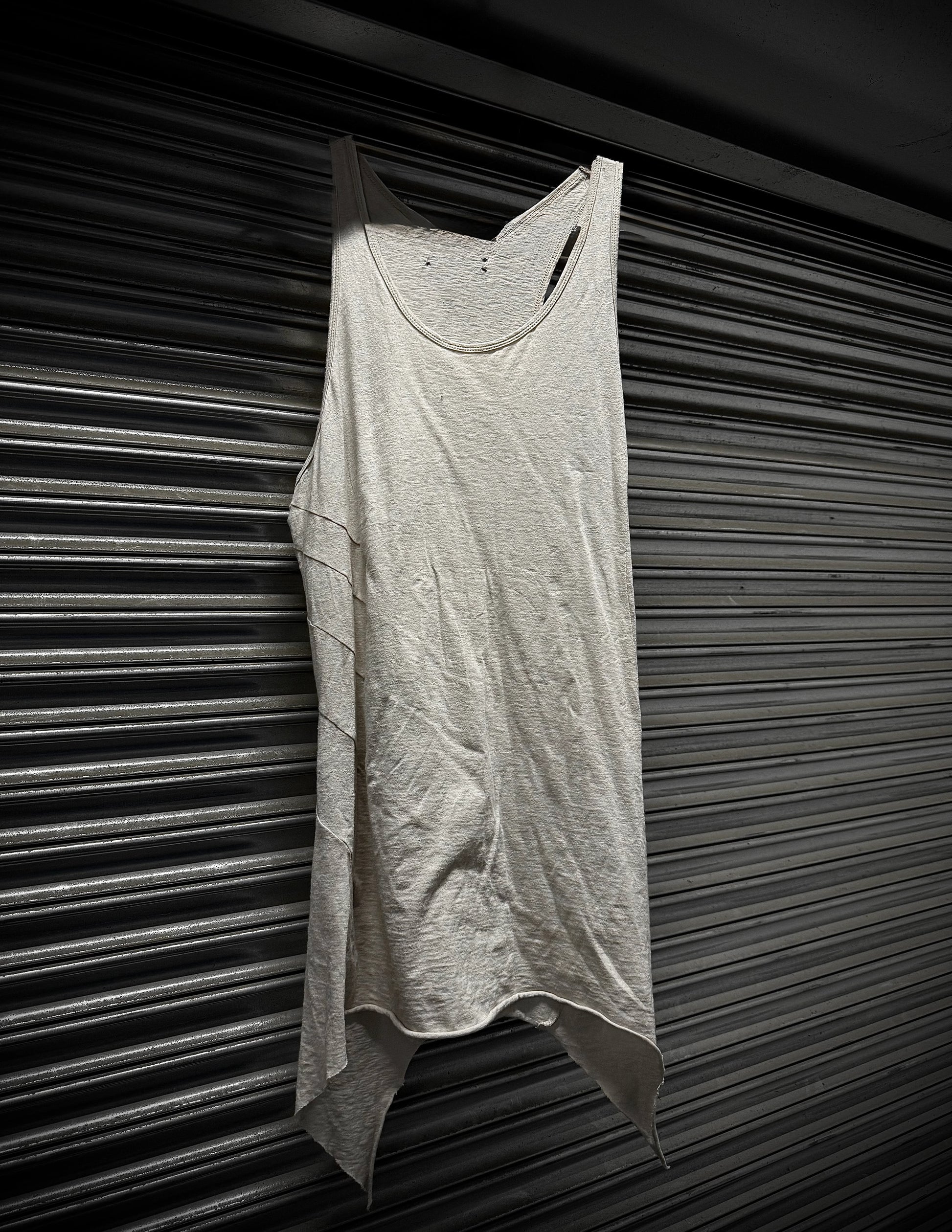Light gray tank top hanging against a dark, textured wall.
