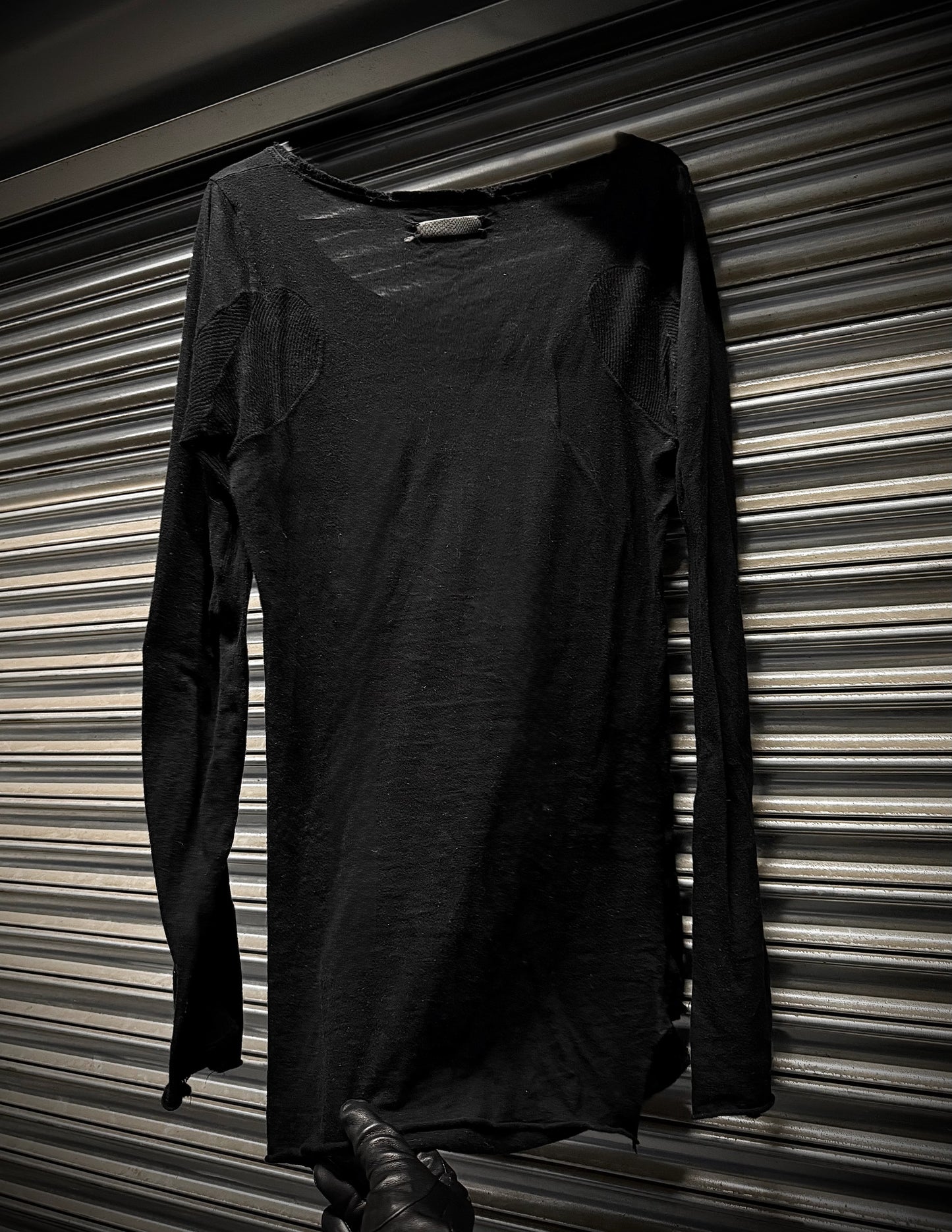 Black long-sleeve dress hanging against a striped wall.