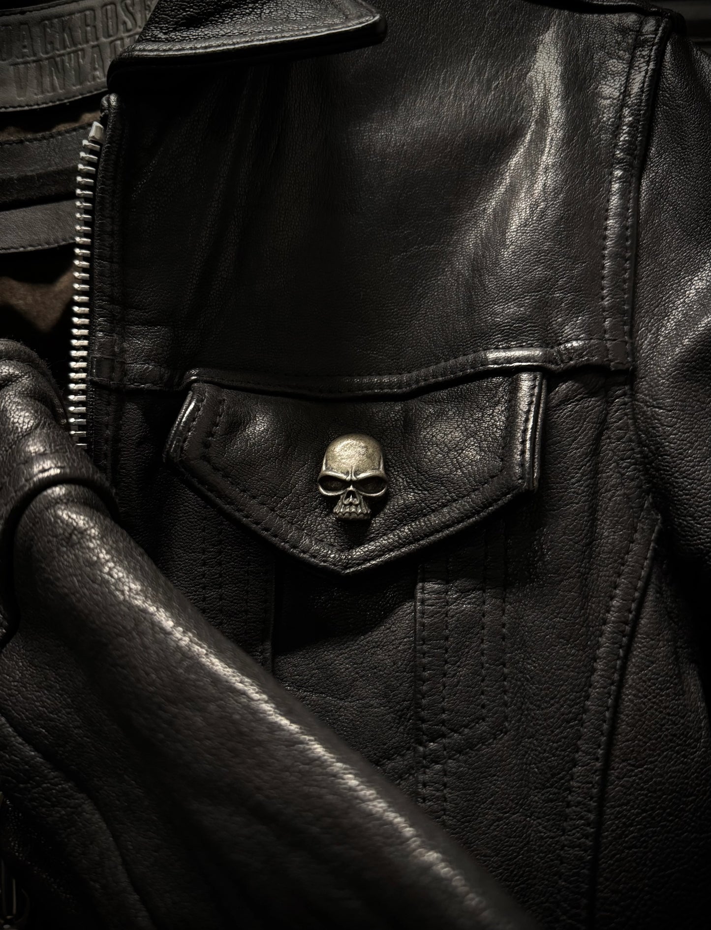 Close-up of a black leather jacket with a skull emblem on a dark background