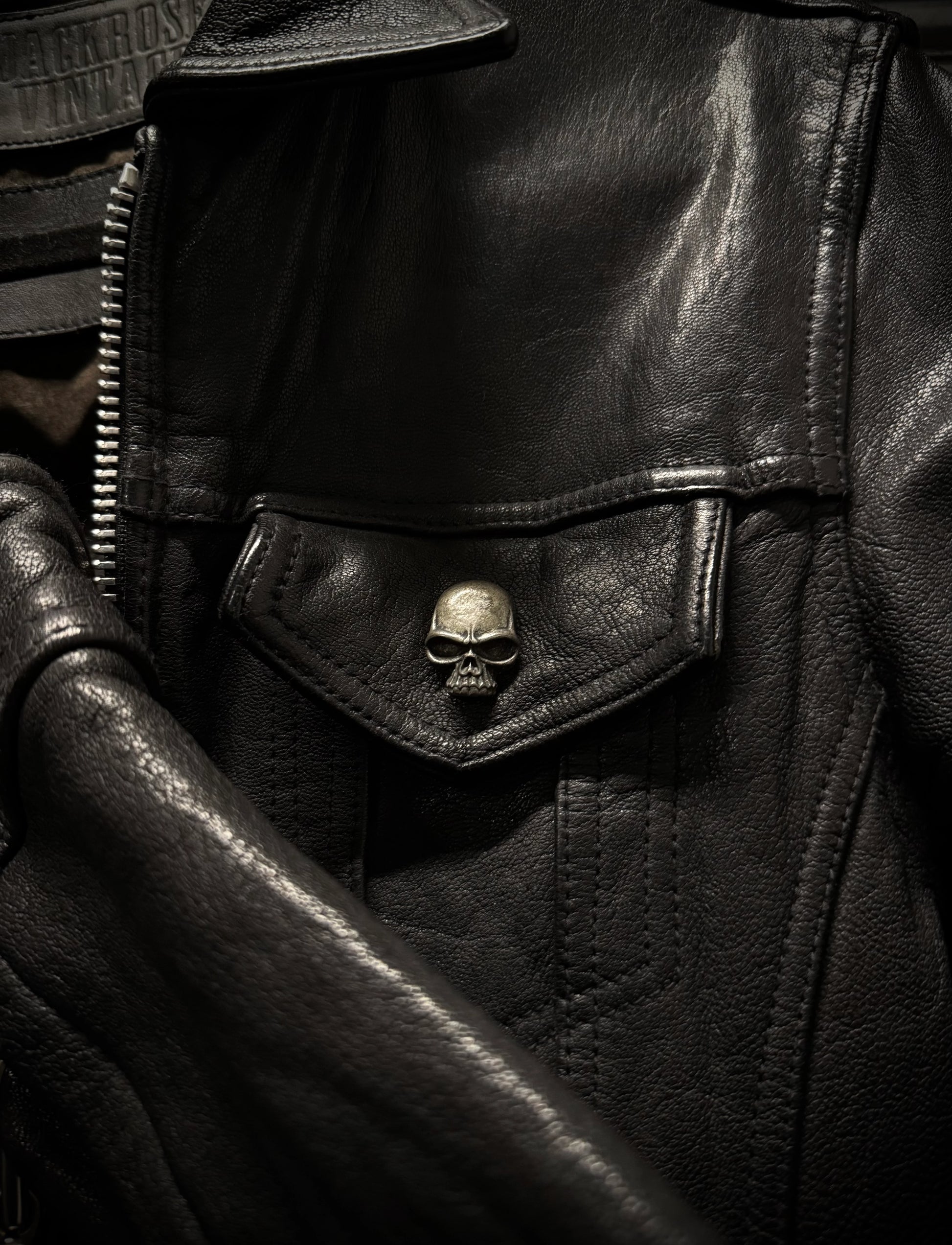 Close-up of a black leather jacket with a skull emblem on a dark background