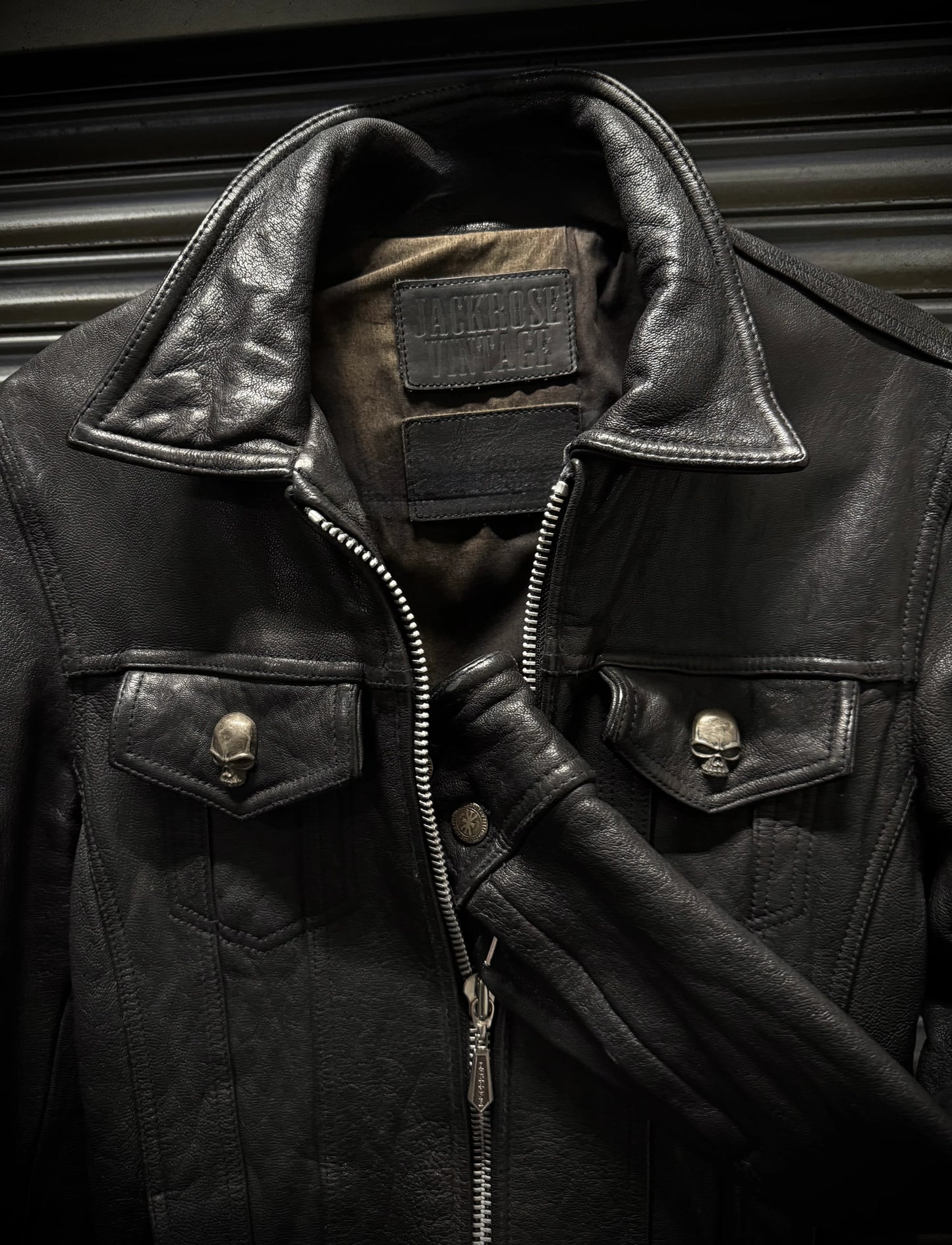 Close-up of a black leather jacket with skull designs on buttons and a patch on a dark background