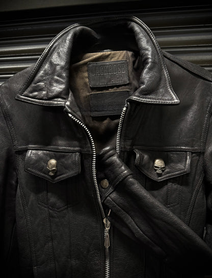 Close-up of a black leather jacket with skull designs on buttons and a patch on a dark background