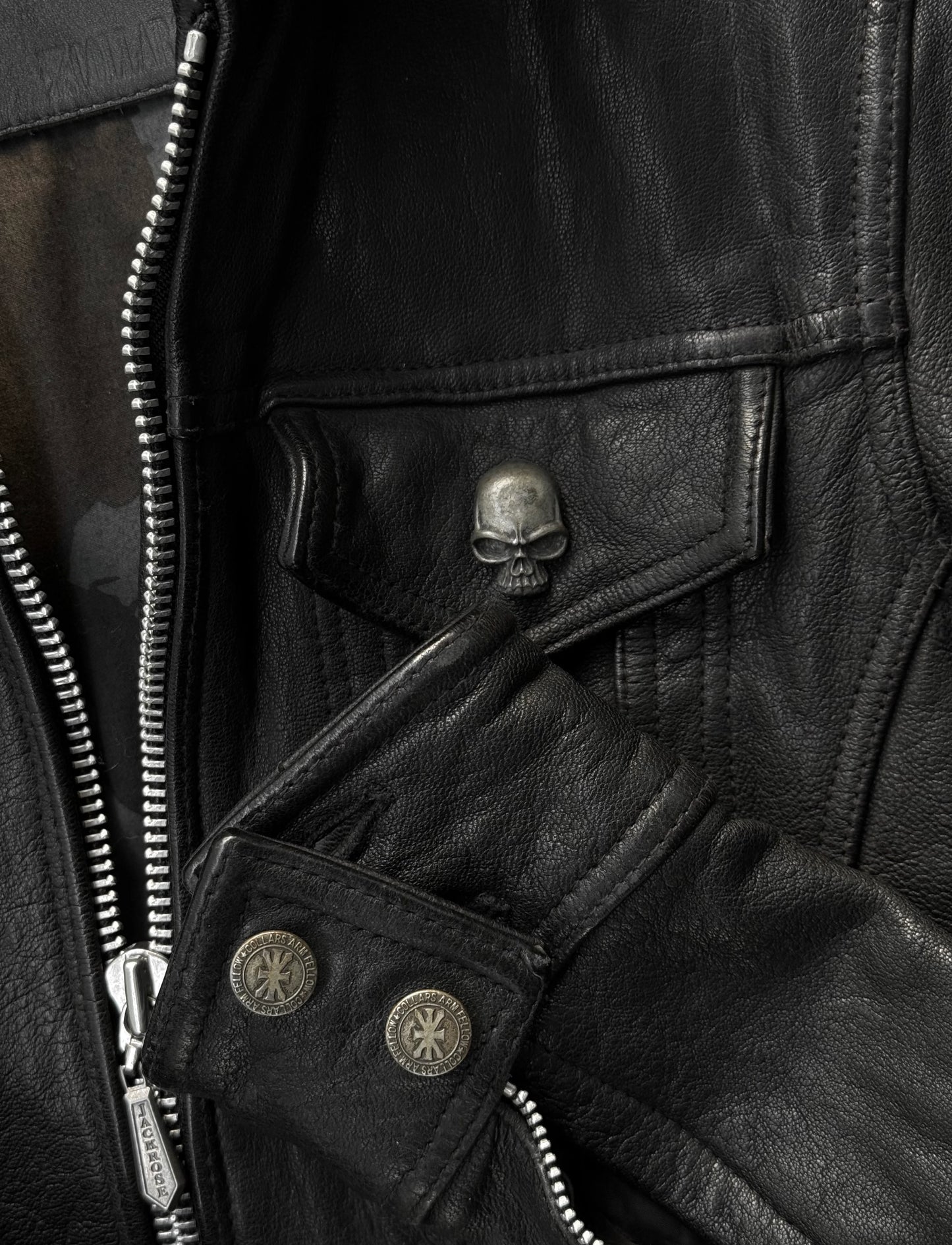 Close-up of a black leather jacket with skull emblem and zipper details.