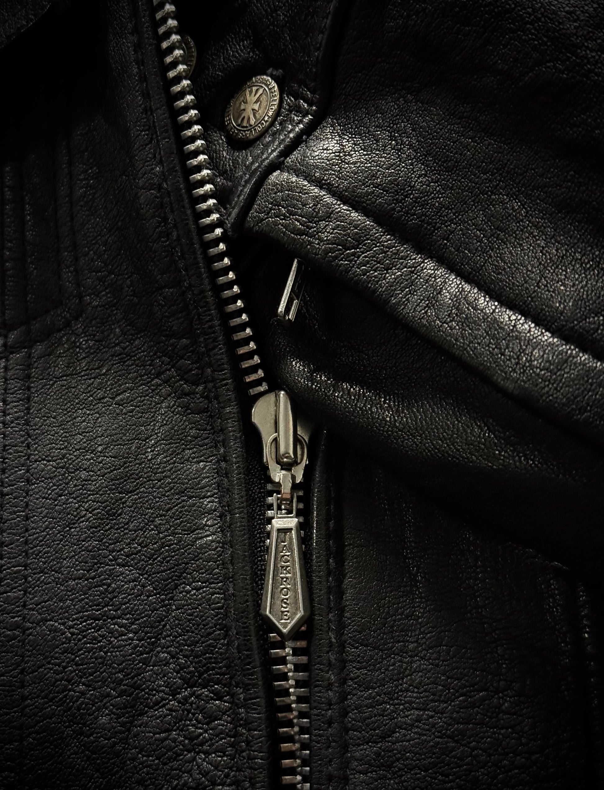 Close-up of a black leather jacket with a zipper and button