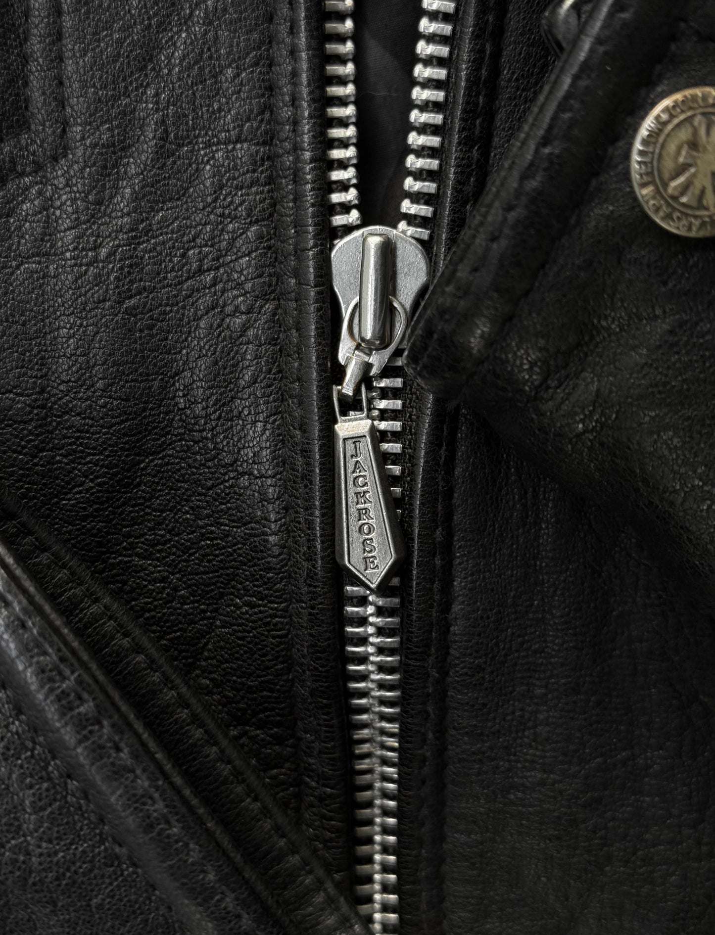 Close-up of a zipper on a black leather jacket with a brand logo.
