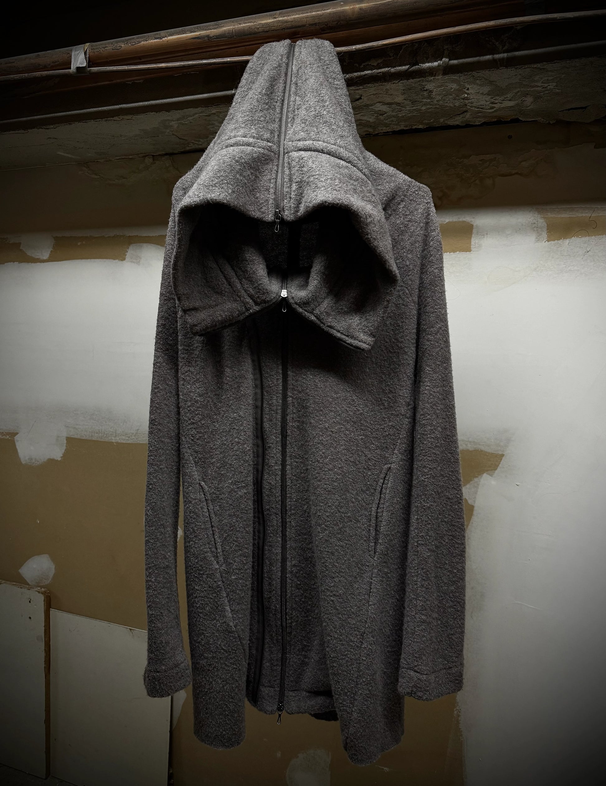 Gray hooded coat hanging against a plain wall.